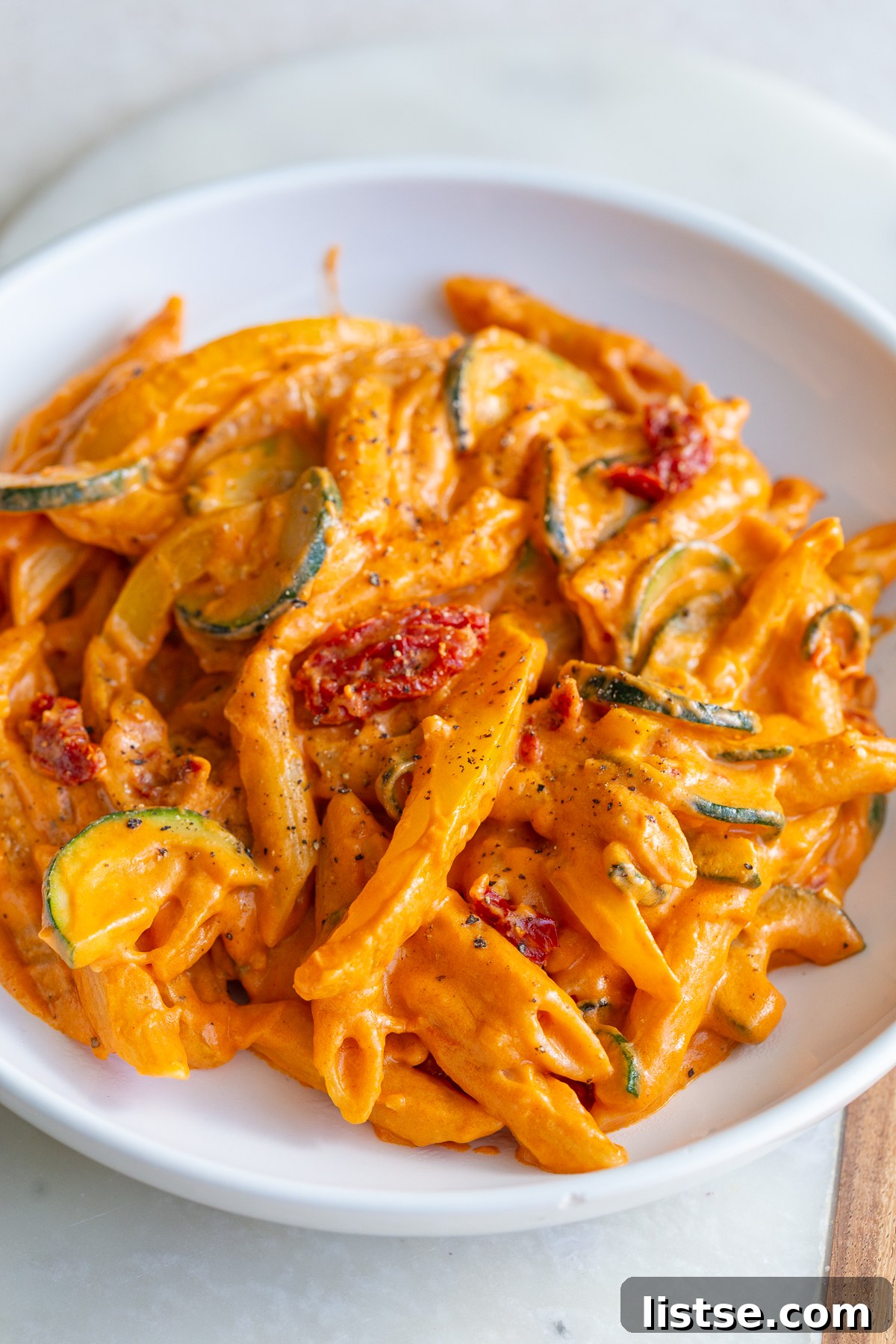 Creamy tomato pasta with bell peppers and zucchini in a white bowl, ready to be served.