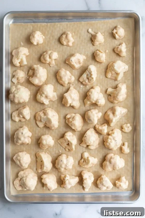 Freshly baked cauliflower wings drizzled with buffalo sauce on a baking sheet.