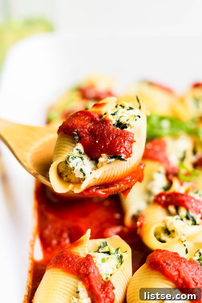 Creamy Vegan Stuffed Shells 3 A single jumbo vegan stuffed pasta shell being lifted with a wooden spoon, showcasing the creamy filling.