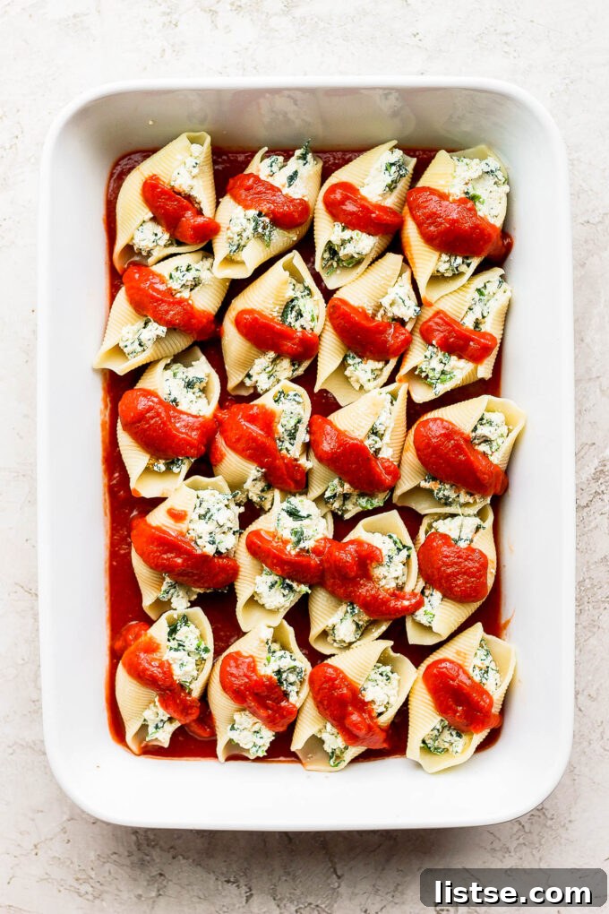 Creamy Vegan Stuffed Shells 7 Marinara sauce being drizzled generously over the stuffed pasta shells in a baking dish.