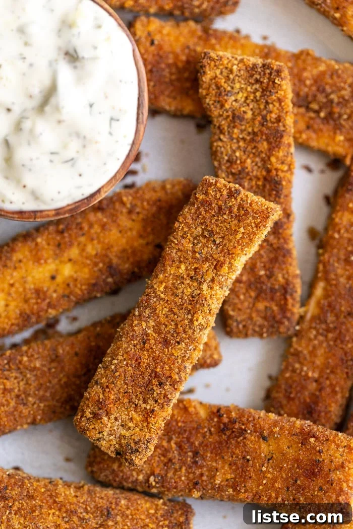 A vibrant platter of crispy tofu fish sticks with fresh lemon wedges and a small bowl of vegan tartar sauce.