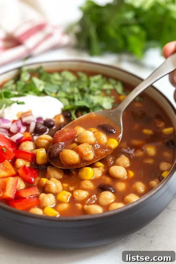 A steaming bowl of chickpea crockpot taco soup, garnished with fresh cilantro and a dollop of vegan sour cream, sits on a rustic wooden table.