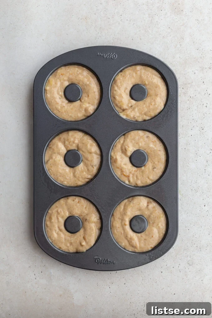 Donut batter neatly piped into a donut baking pan, showing the distinct ring shapes.