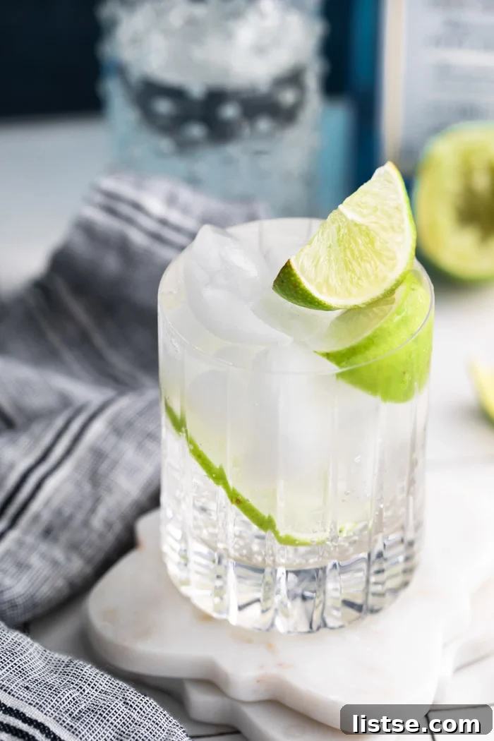 clear beveled glass filled with clear liquid (gin and tonic) plus fresh lime wedges towel on the side