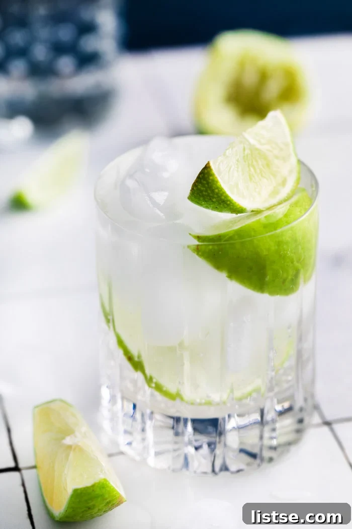 clear beveled glass filled with clear liquid (gin and tonic) plus fresh lime wedges
