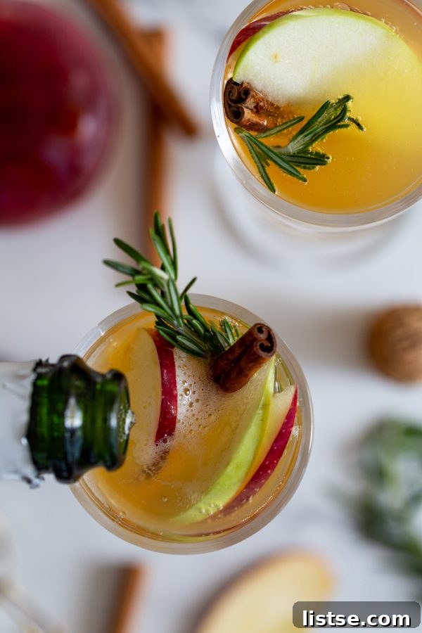 Close-up of an Apple Cider Mimosa in a flute glass, garnished with a cinnamon stick, rosemary sprig, and apple slice, showing off its inviting color and bubbles.
