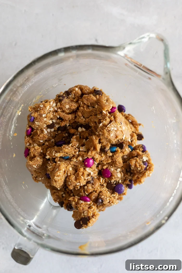 Close-up of vegan monster cookie dough mixed with chocolate chips and candies in a bowl.