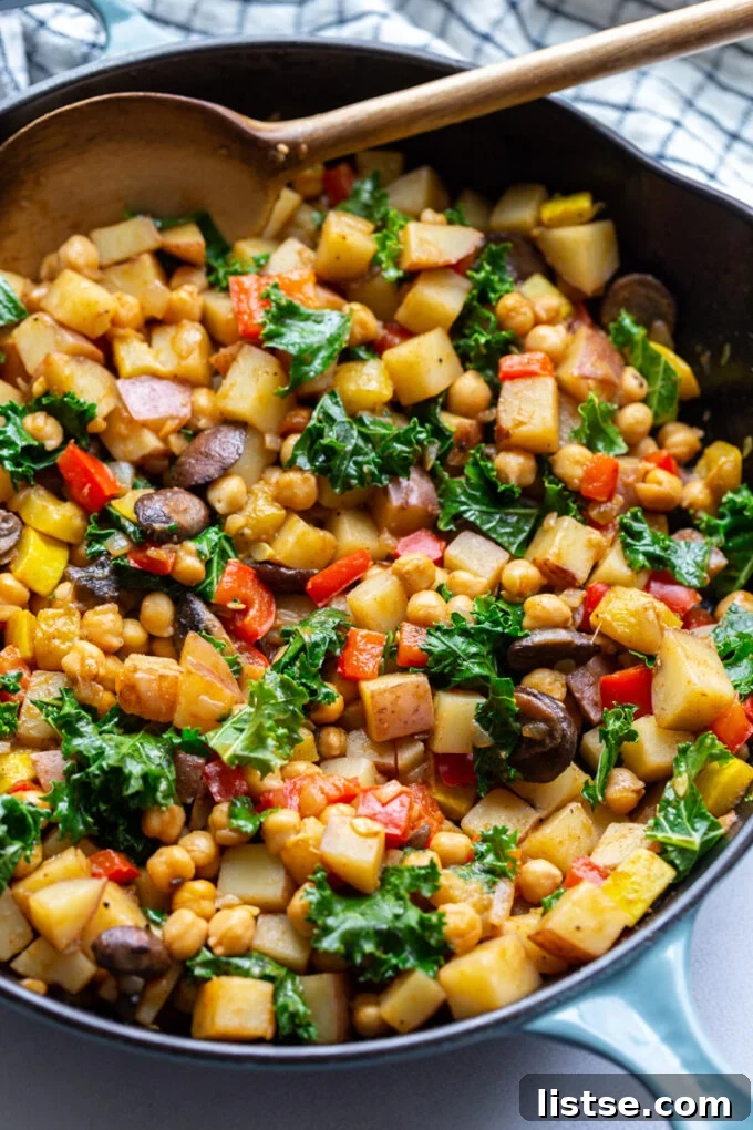 A wooden spoon stirring potatoes and mixed vegetables in a large skillet