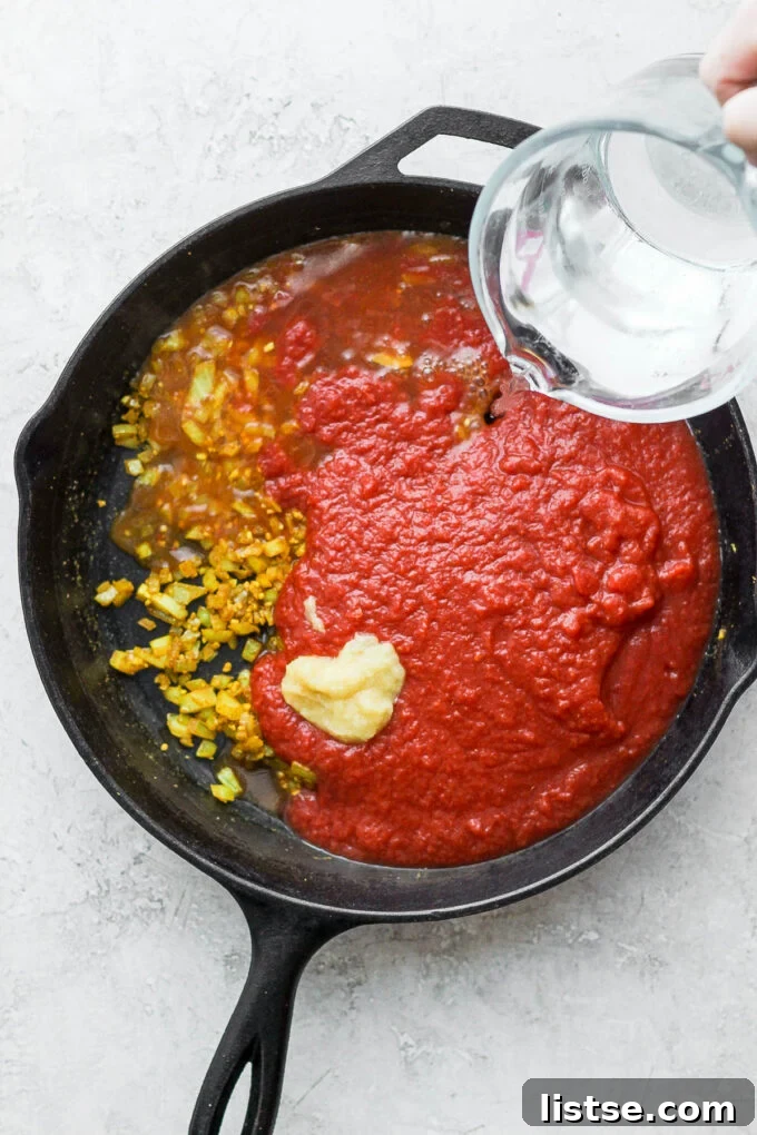 Adding water to a mixture of lentils and crushed tomatoes in a skillet.