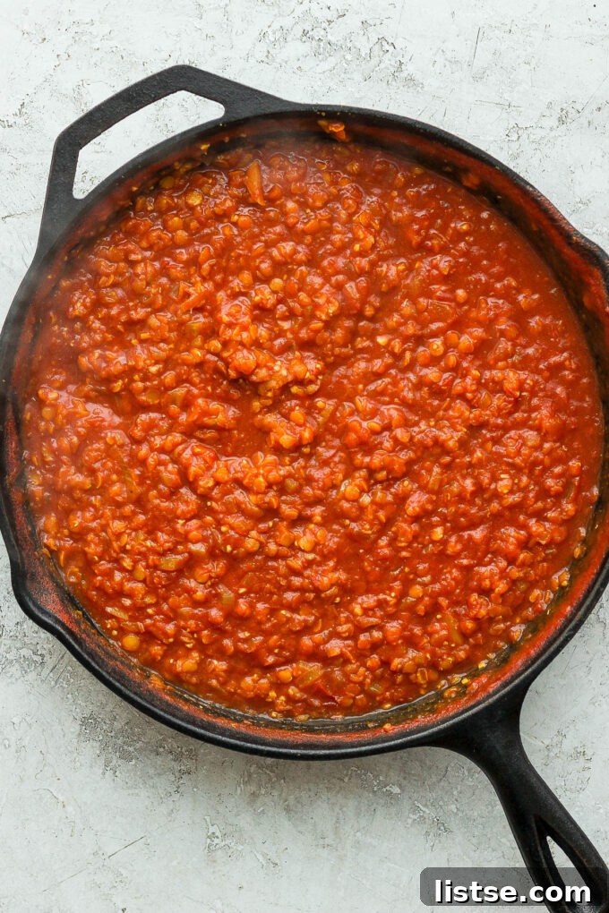 A skillet filled with the simmering lentil and tomato mixture.