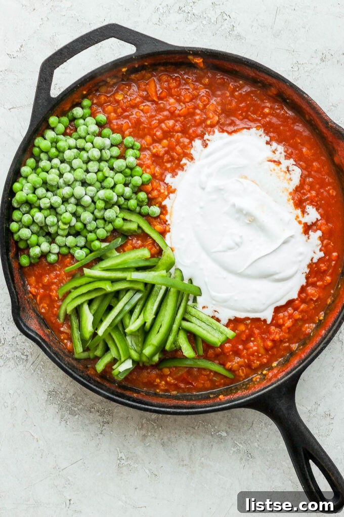 Adding frozen peas, sliced bell pepper, and coconut milk to the lentil curry.