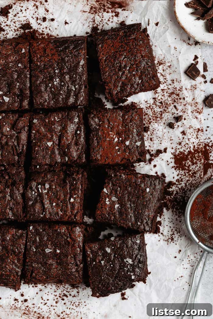 Easy vegan brownies on a white backdrop with a light dusting of cocoa powder.