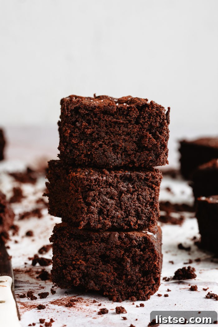 Three decadent vegan brownies stacked on a white background, showcasing their thick, fudgy texture.