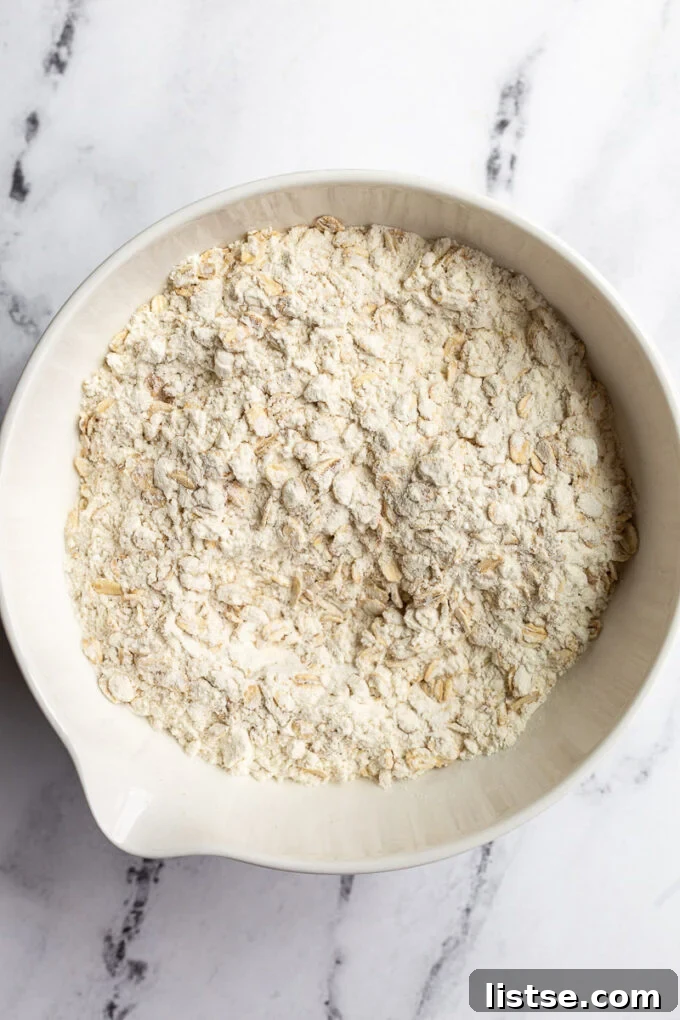 Dry ingredients for vegan oatmeal cookies, including flour and oats, perfectly measured in a large white mixing bowl.