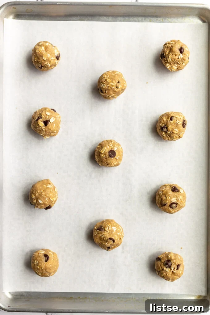 Portioned vegan oatmeal cookie dough balls neatly arranged on a baking tray, ready for chilling and baking.