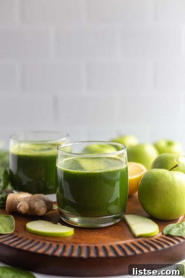 Green Apple Revival 2 Two glasses of vibrant green juice on a wooden board, garnished with fresh apple slices and ginger, ready to be enjoyed.