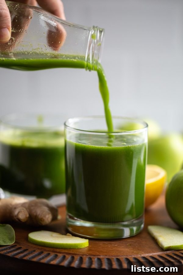 Green Apple Revival 6 Freshly pressed apple green juice being poured into a small elegant glass on a wooden board, showcasing its vibrant color.