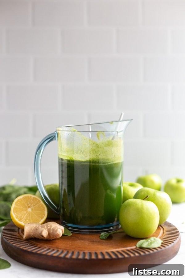 Green Apple Revival 7 A large glass pitcher filled with vibrant freshly squeezed green juice, placed on a wooden board against a clean white background.