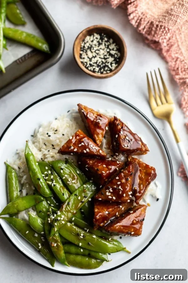 Tempeh Smokehouse Bowls 4 smoked tempeh pieces and sugar snap peas on top of white rice in a bowl, sprinkled with sesame seeds for garnish