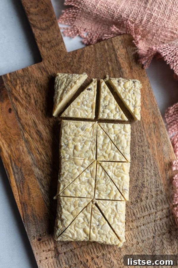 Tempeh Smokehouse Bowls 5 block of tempeh on a wood board, partially cut into small triangles to show the slicing process