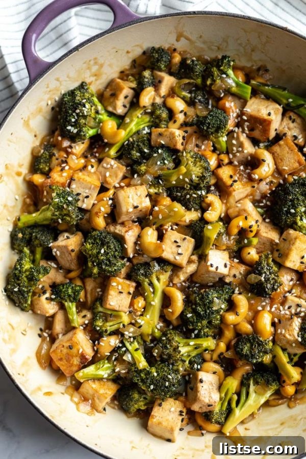 Tofu stir fry sizzling in a large skillet, showcasing the cooking process before adding the cashews and sauce.
