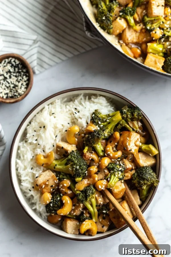 A close-up of cashew tofu stir fry served in a bowl over white rice, showcasing the rich sauce and vibrant ingredients.