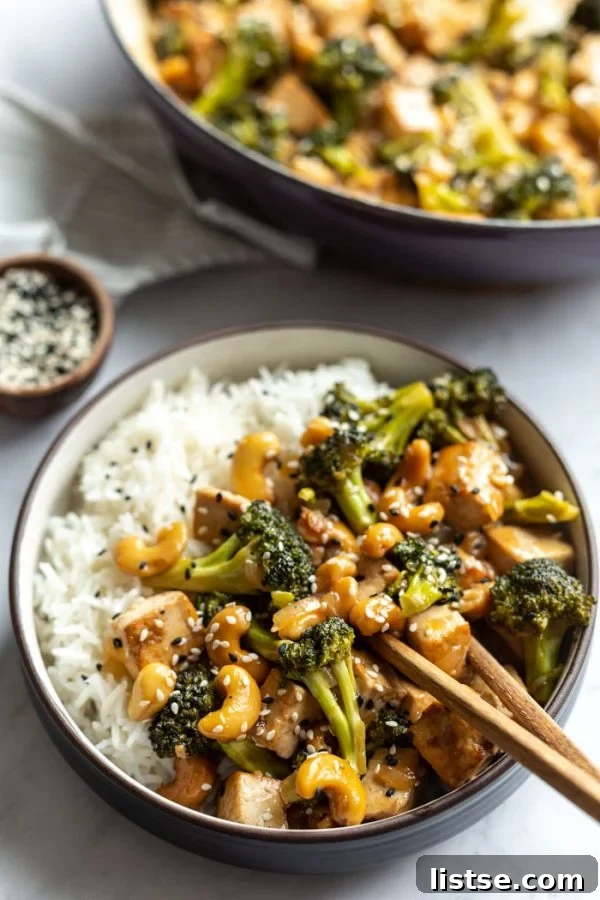 A bowl of cashew stir fry with tofu and broccoli, served over white rice with chopsticks, inviting a flavorful meal.