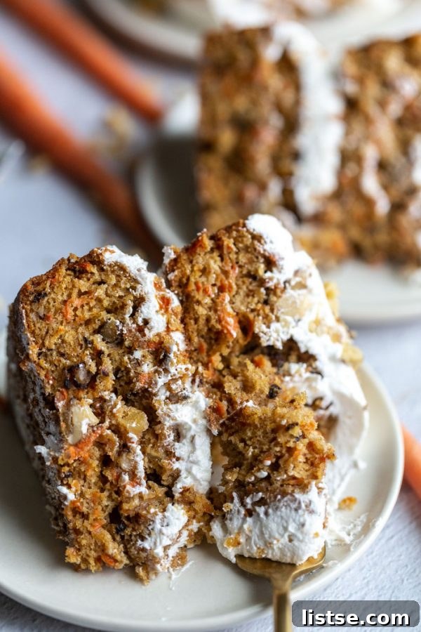Close-up shot of a slice of vegan carrot cake with a bite taken out, showing the moist crumb and frosting
