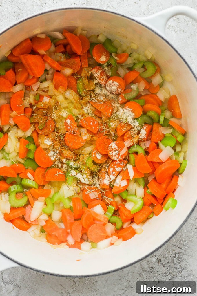 Golden Chickpea Noodle Hug 4 Chef sautéing a colorful mix of onions, celery, and carrots in a large pot with olive oil.