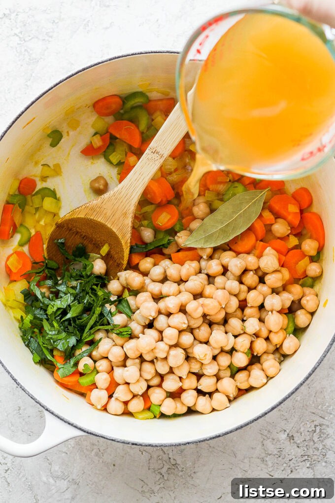 Golden Chickpea Noodle Hug 5 Adding vegetable broth to the pot with sautéed vegetables, chickpeas, and spices for soup.