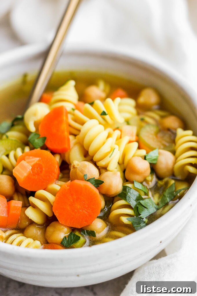 Golden Chickpea Noodle Hug 9 A close-up shot of a comforting bowl of chickpea noodle soup with a spoon, ready to be eaten.