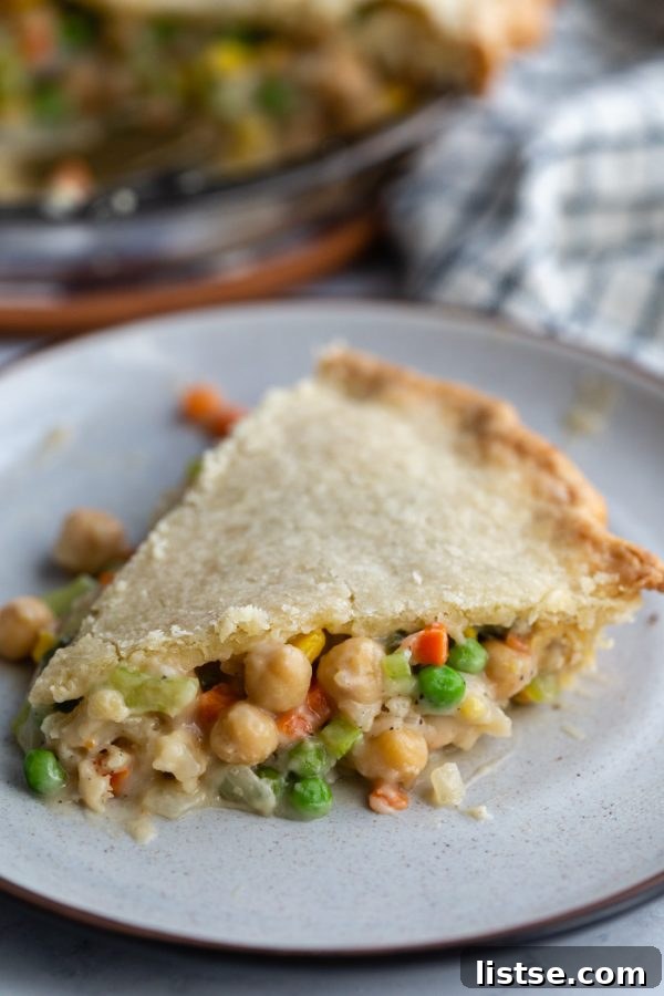 Hearty Vegan Chickpea Pot Pie 3 A generous slice of vegan chickpea pot pie on a white plate, revealing the rich, chunky filling of chickpeas and mixed vegetables.