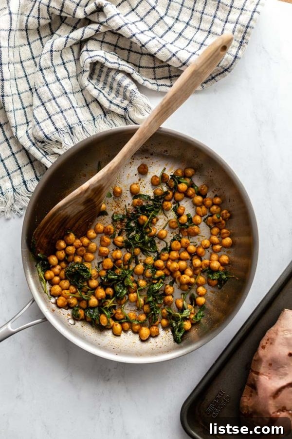 top down shot of chickpeas and wilted arugula in a frying pan with a napkin in the corner