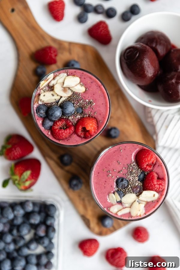 Top-down shot of a radiant pink beet smoothie, beautifully garnished with fresh raspberries, crunchy chia seeds, delicate almond slices, and plump blueberries.