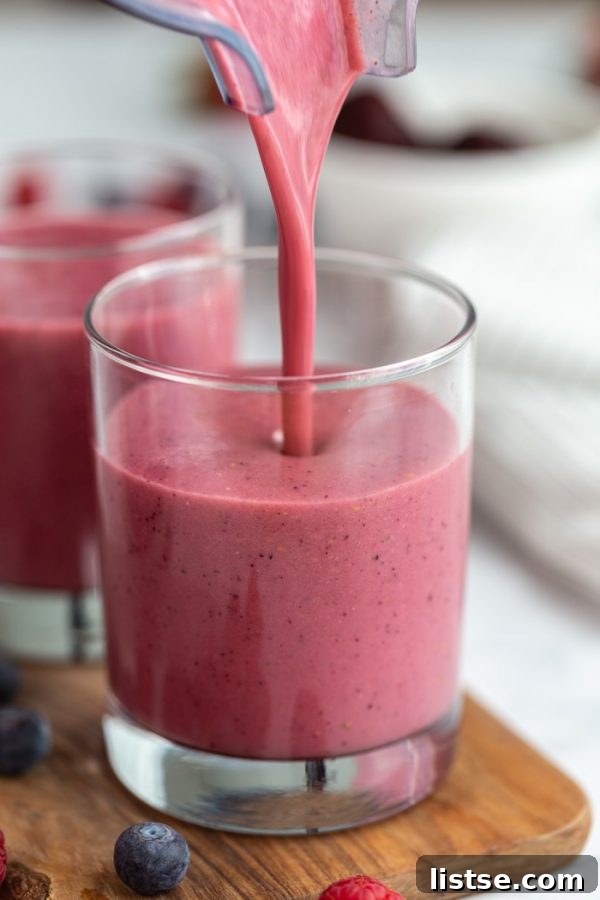 A stream of rich, dark pink smoothie elegantly pouring into a small, clear glass, showcasing its luscious texture and inviting color.