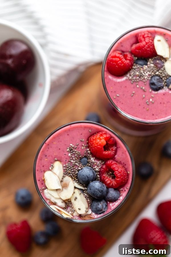 A stunning top-down shot of two bright pink beet smoothies, elegantly garnished with a medley of fresh fruit, crunchy chia seeds, and delicate almond slices, ready to be enjoyed.