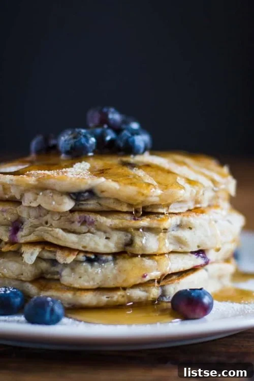 Stack of fluffy vegan blueberry pancakes topped with fresh berries and drizzled with syrup