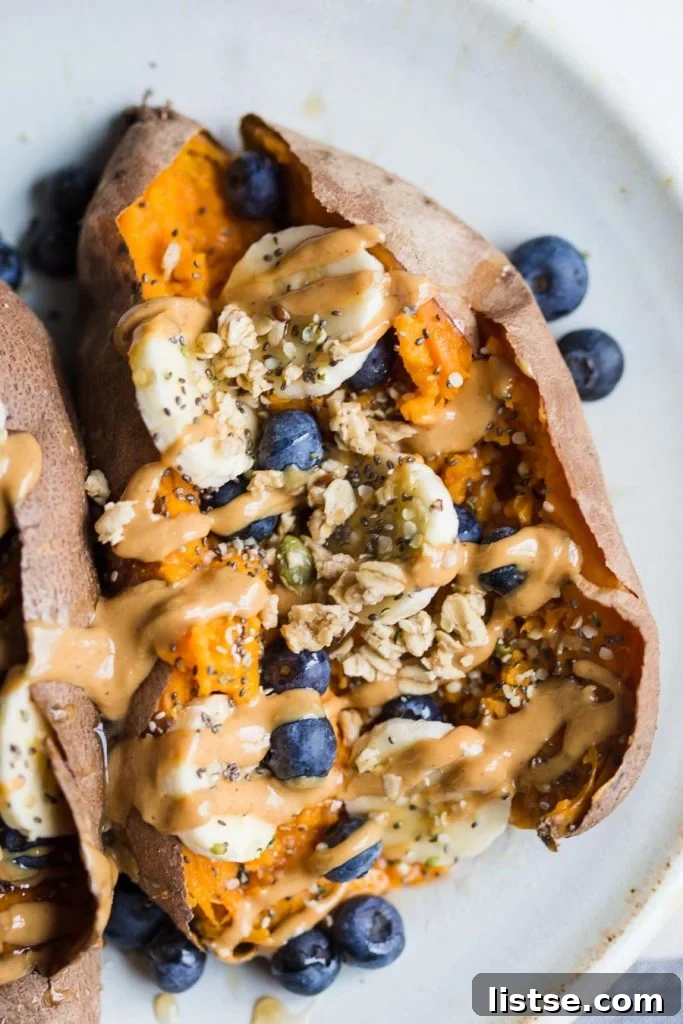 up close shot of a cooked sweet potato split open with sliced banans, blueberries, granola and peanut butter on it
