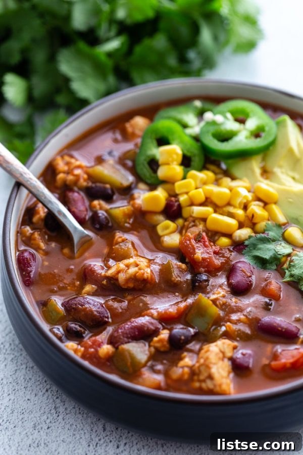 Close-up shot of a vibrant bowl of tempeh chili garnished with bright green cilantro, a dollop of vegan sour cream, and a slice of fresh lime, ready for serving.