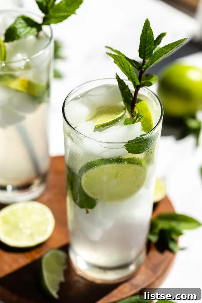 Two refreshing mojitos, perfectly chilled in tall glasses, adorned with vibrant lime slices and crisp mint sprigs. The glasses rest on a round wooden serving board.
