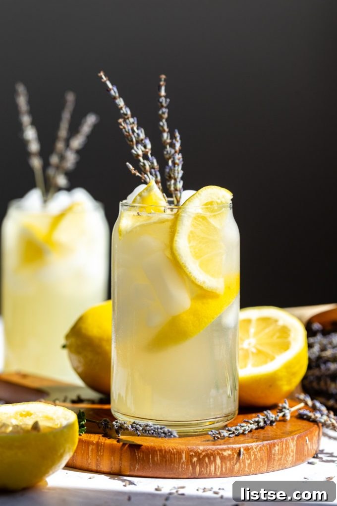 glass of vodka lemonade with slices of lemon and lavender in it. sitting on a wood board with a black background