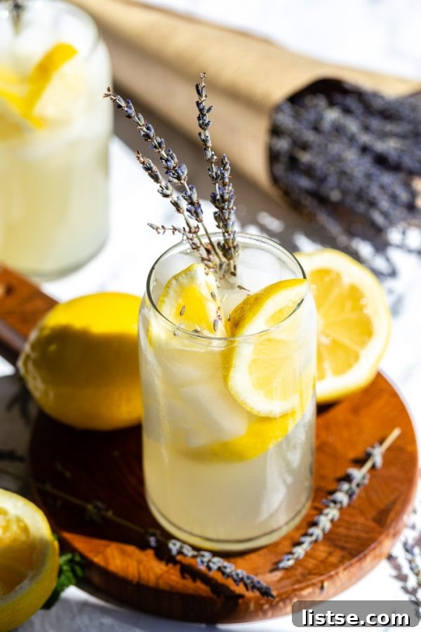 glass of lemonade with slices of lemon and lavender in it. sitting on a wood board with lemons and lavender all around it