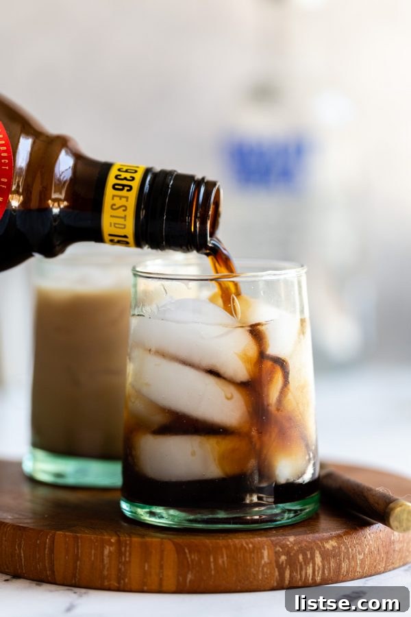 Crafting the Perfect White Russian 3 small cup of a white russian: black liquid on ice with kahlua being poured into the glass