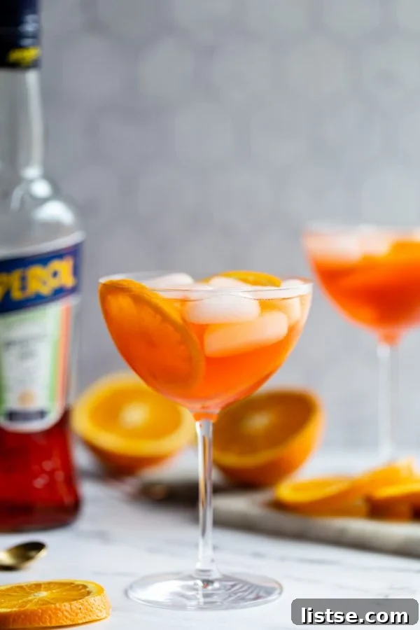 Timeless Aperol Spritz 2 Vibrant orange Aperol Spritz in a wine glass, garnished with an orange slice, set against a marble backdrop with scattered oranges and an Aperol bottle in soft focus.