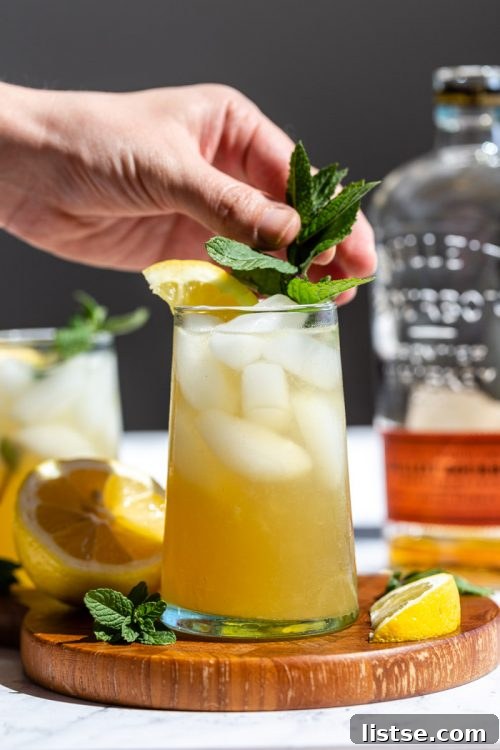 A frosty Whiskey Smash cocktail served in a classic rocks glass with a generous amount of ice, garnished with fresh mint and lemon slices.
