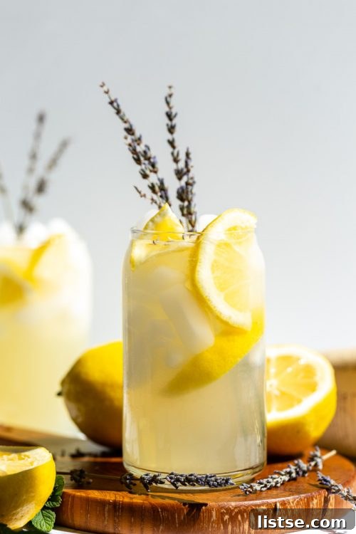 A beautiful Lavender Vodka Lemonade cocktail in a tall glass, garnished with a sprig of fresh lavender and a lemon slice, exhibiting a soft purple color.