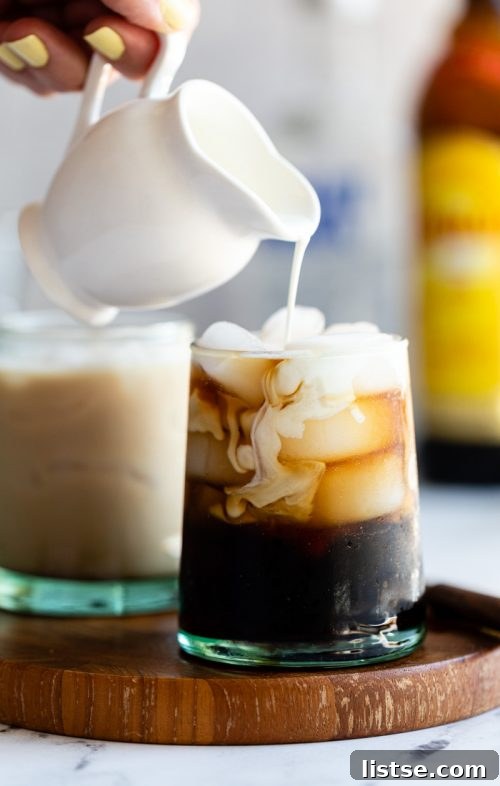 A rich and creamy White Russian cocktail, showcasing layers of coffee liqueur and fresh cream, served over ice in a wide rocks glass.