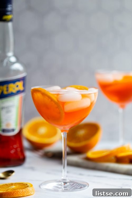 An inviting Aperol Spritz cocktail in a large stemmed wine glass, adorned with a fresh orange slice and filled with sparkling, ice-cold liquid.