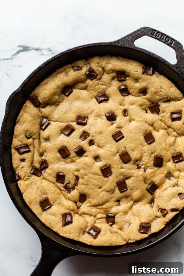 top down shot of black cast iron skillet with a skillet cookie in covered in chocolate chunks. On a marble background 