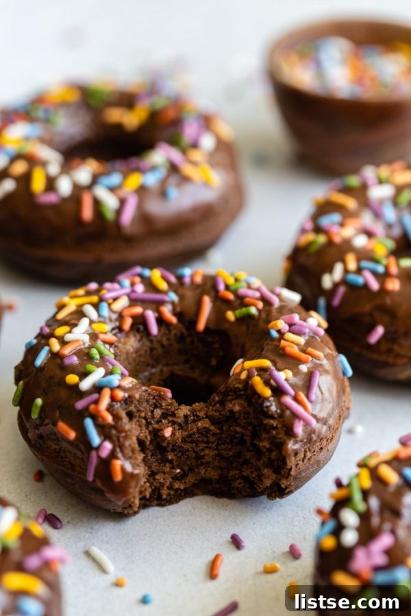 No-Fry Chocolate Donuts 2 chocolate glazed donuts topped with sprinkles and sprinkles all around the shot. The main donut in the shot has a bite taken out